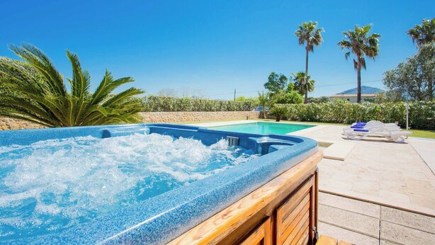Un bain à remous avec une structure en bois, une piscine et des chaises longues, le tout dans un cadre extérieur ensoleillé.