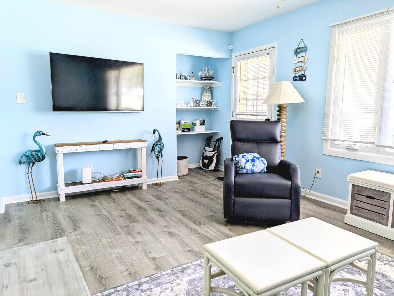 A living room with a flat-screen TV, a black leather chair, a white console table, and a bookshelf with decorative items.