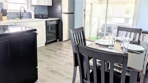 A compact kitchen with white cabinets, a black refrigerator, and a dining table set for four. - Cozy White Cottage by the Bay (Lower Township)