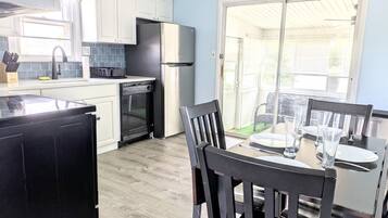 A compact kitchen with white cabinets, a black refrigerator, and a dining table set for four.