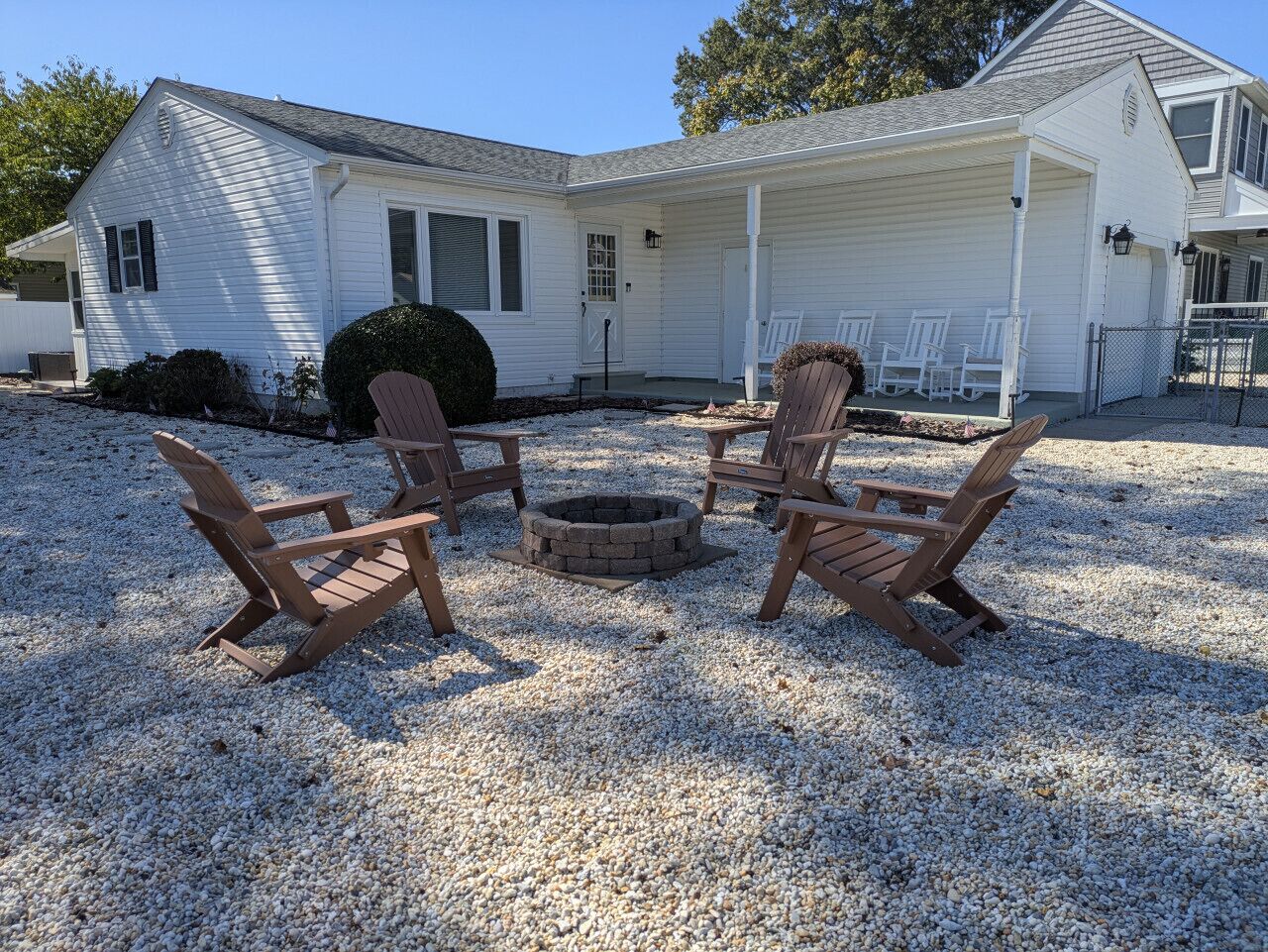 A house with a covered porch, a fire pit, and four Adirondack chairs.