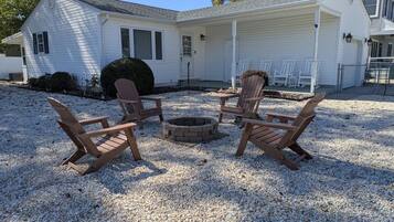 A house with a covered porch, a fire pit, and four Adirondack chairs.