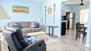 A living room with a sofa, coffee table, and a dining area with chairs and a table. - Cozy White Cottage by the Bay (Lower Township)