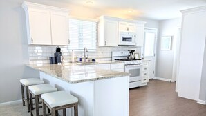 A modern kitchen with white cabinetry, a granite countertop, and a built-in island with bar stools. - Summer Breezes, Bay Views (Lower Township)