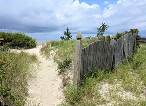A sandy path leading to a wooden fence with a decorative post.