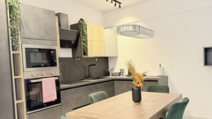 A modern kitchen with built-in appliances, a dining area with a wooden table and green chairs, and a pendant light. - P071 – Porto Recanati, Three-Room Apartment with Garden and Wi-Fi (Porto Recanati)