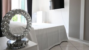 A hotel room with a bed, a TV mounted on the wall, and a decorative crystal mirror on a table. - P071 – Porto Recanati, Three-Room Apartment with Garden and Wi-Fi (Porto Recanati)