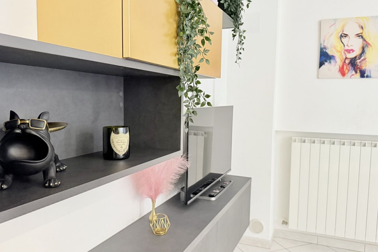 A modern kitchen with a black countertop, a gold cabinet, a black piggy bank, a gold vase, and a pink feather.