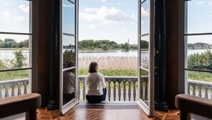A room with large windows offering a view of a lake and surrounding greenery. - Paviljoen De Notelaer (Bornem)