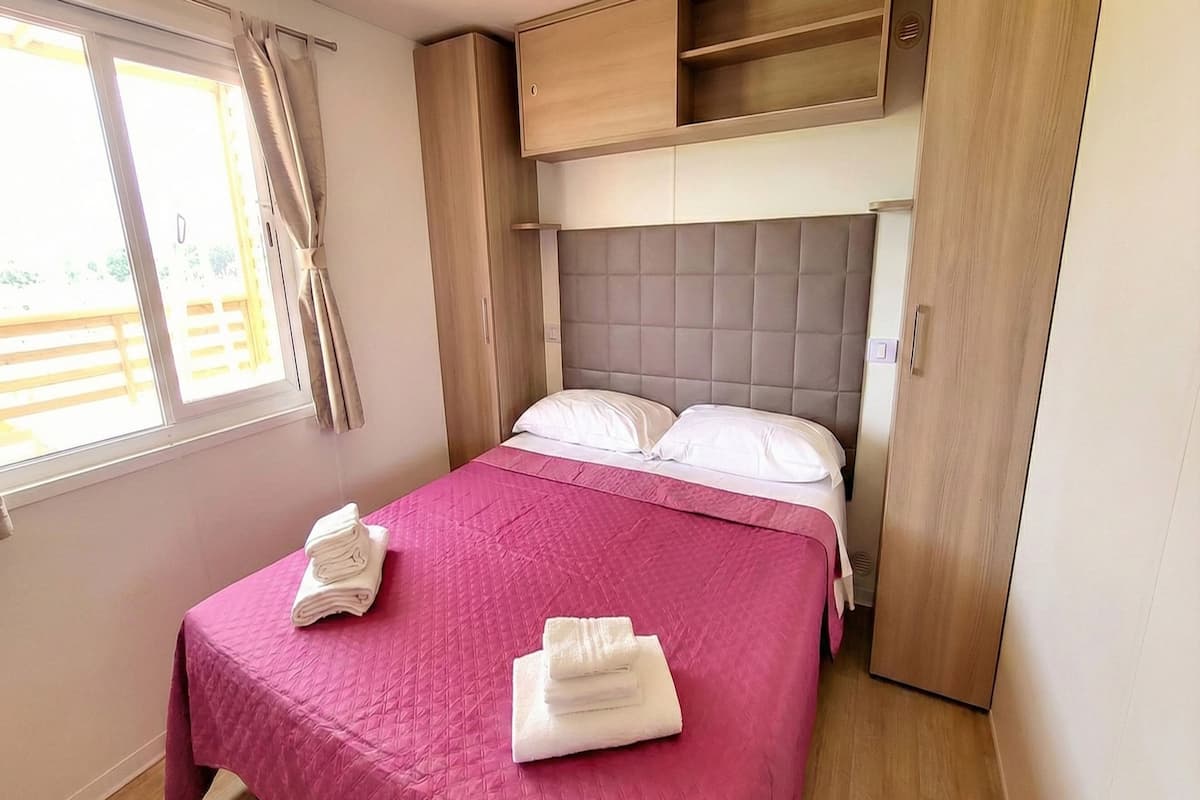 Une chambre à coucher avec un lit, des oreillers, une couvre-lit rose et deux serviettes blanches pliées.