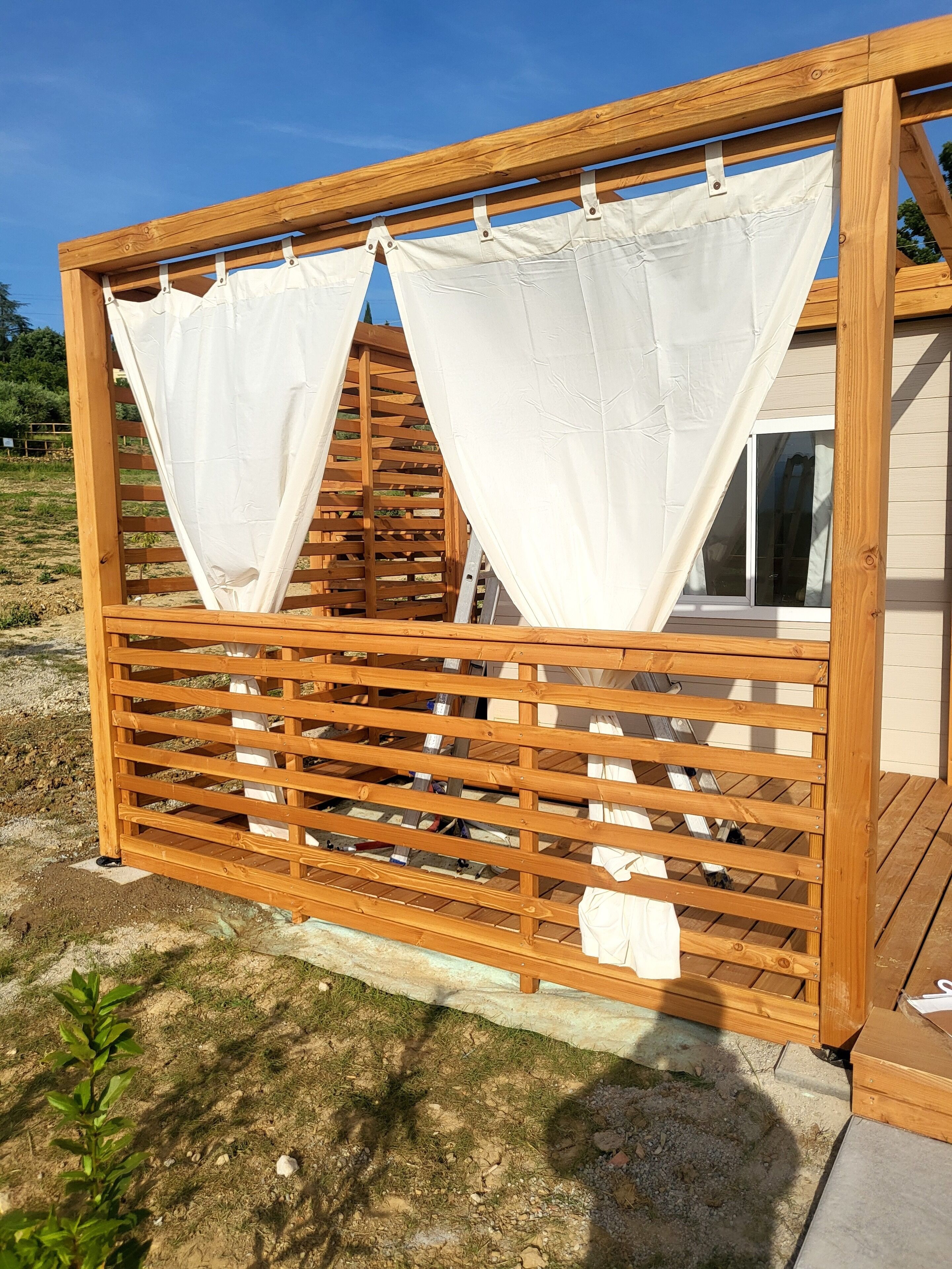 A wooden structure with a lattice design and white curtains.