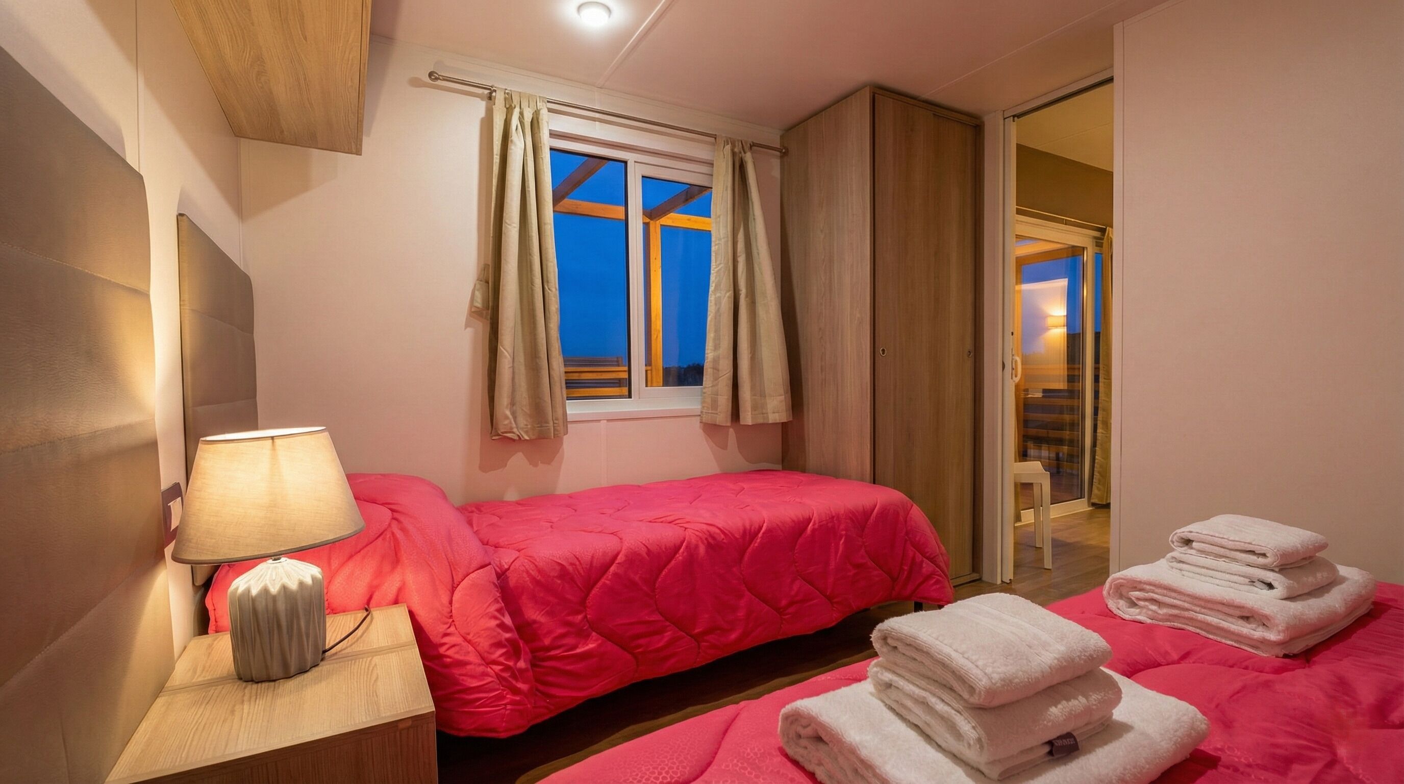 Une chambre à coucher comprenant un lit, une table de chevet, une lampe, une fenêtre avec des rideaux et une vue sur l’extérieur.