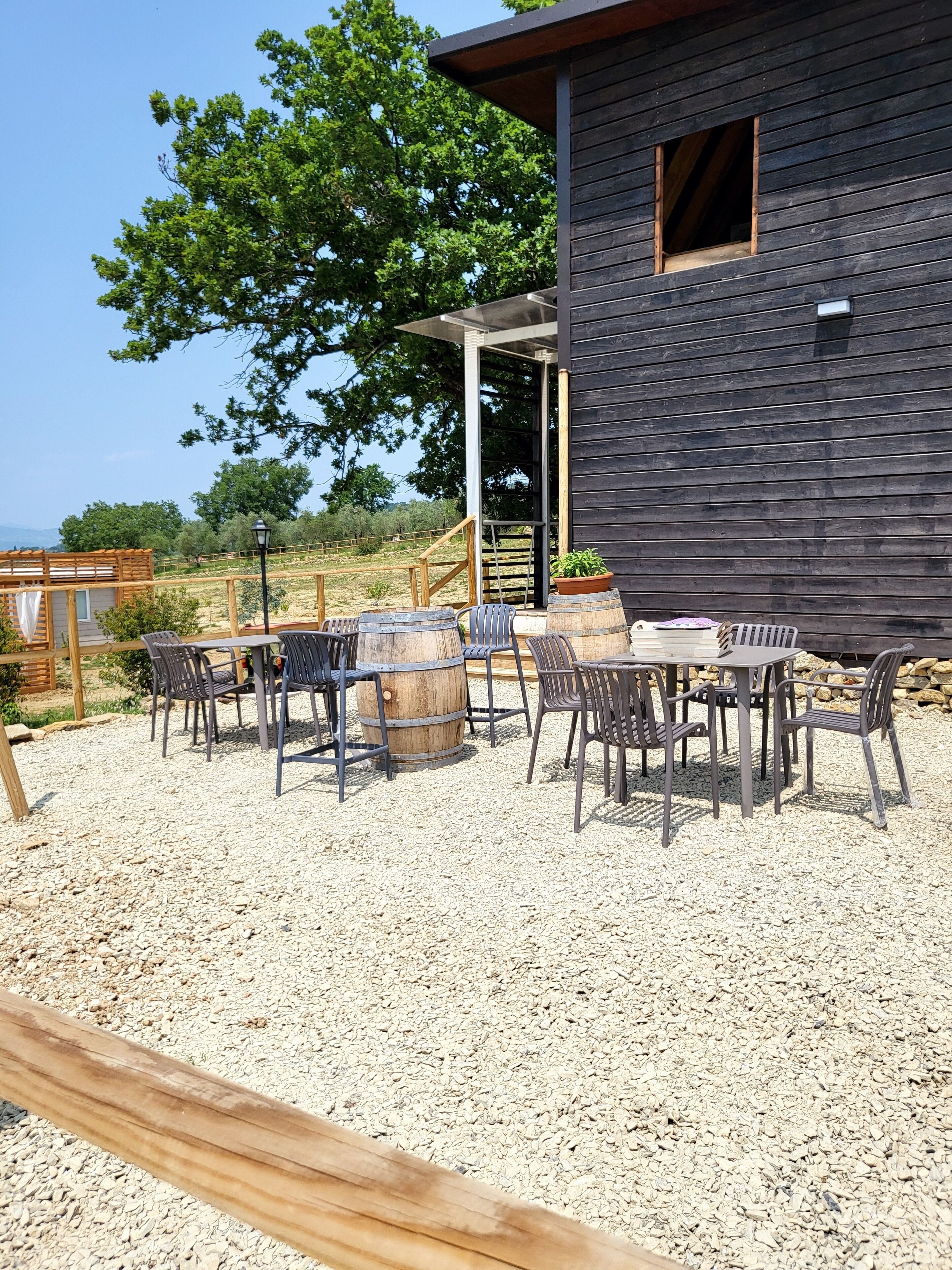A rustic outdoor seating area with a wooden table and chairs, a barrel, and a pergola structure.