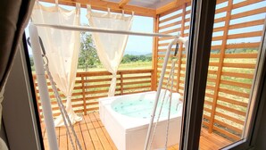 A wooden deck with a hot tub, a swing chair, and a view of the countryside.