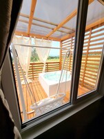 A wooden deck with a hot tub, a swing chair, and a view of the countryside.