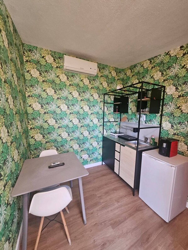 Une cuisine compacte comprenant un coin repas, un petit réfrigérateur et une étagère intégrée.