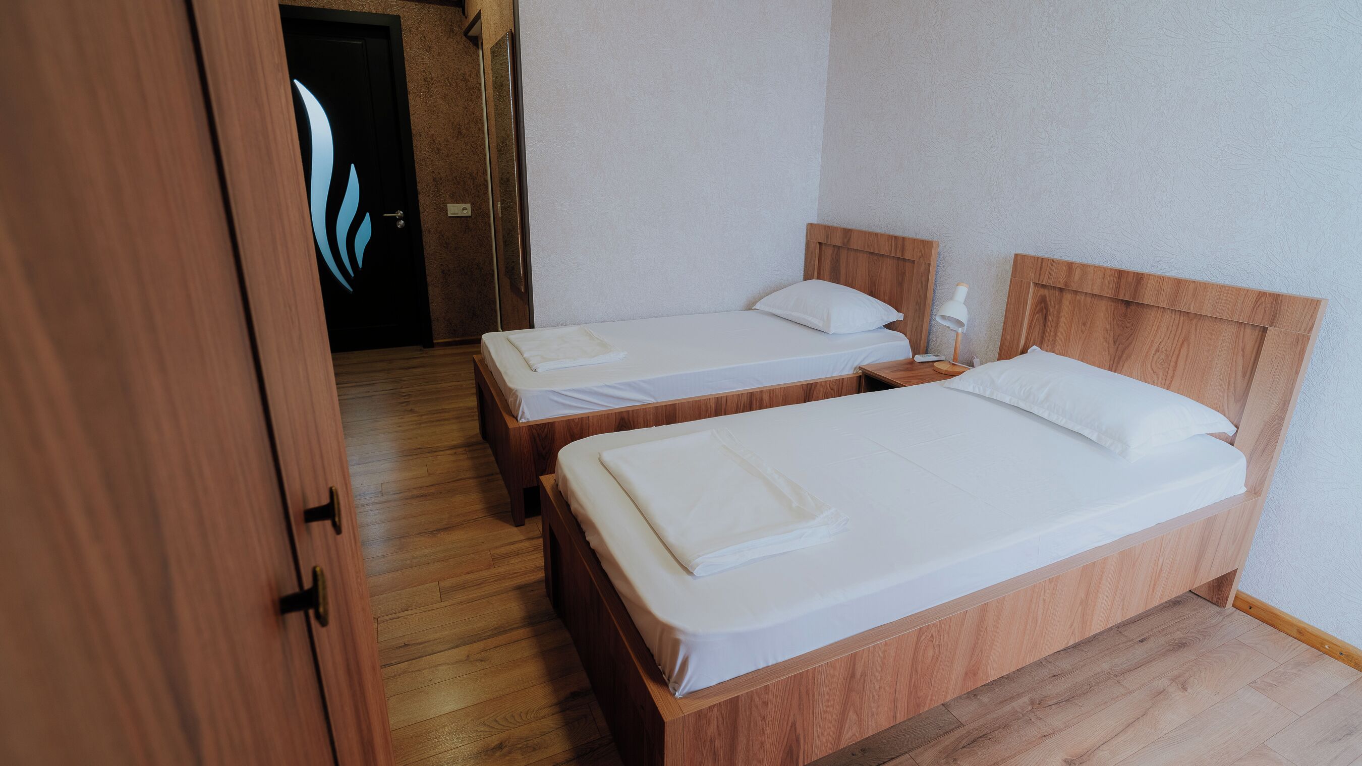 A hotel room with two wooden beds, a wooden wardrobe, and a wooden floor.