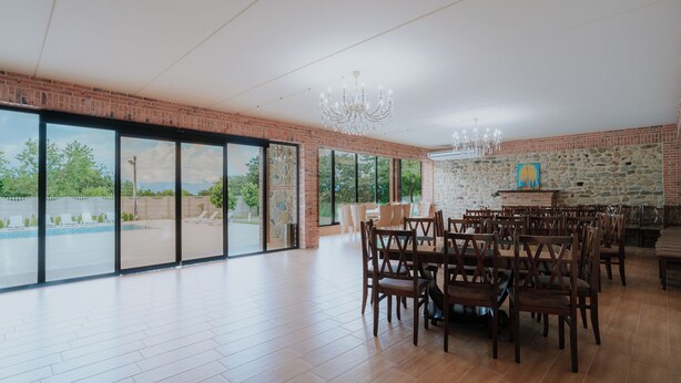 A spacious dining area with large windows, a stone wall, and a chandelier. - Villa Ikalto (Telavi)