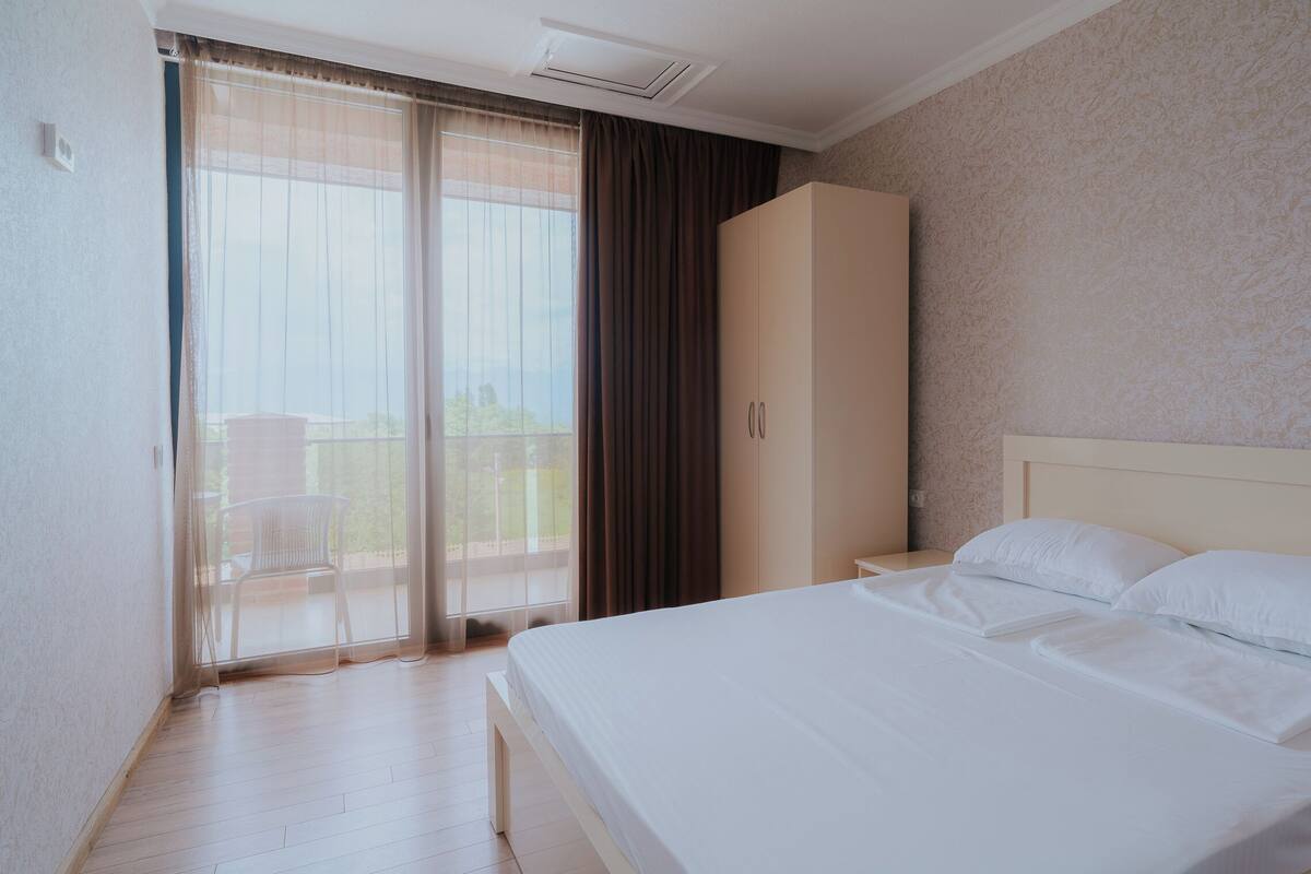 A hotel room with a bed, a wardrobe, and a sliding glass door leading to a balcony.