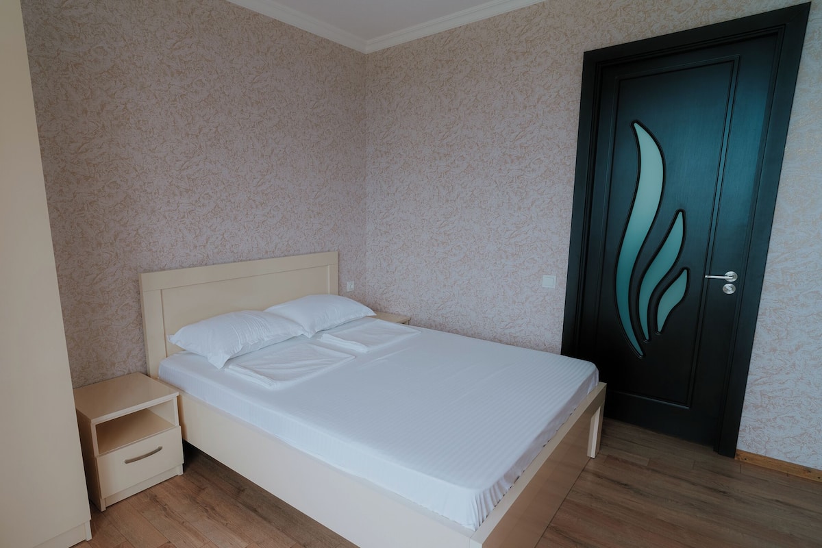 A bedroom with a bed, a nightstand, a wardrobe, and a door.