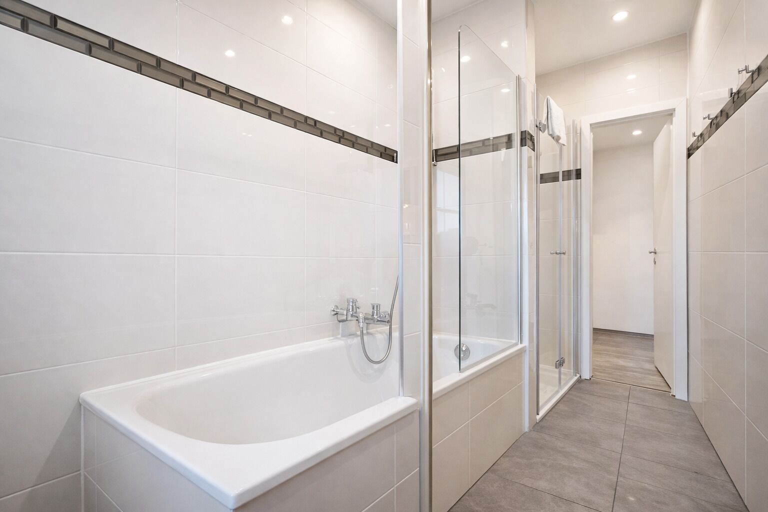 A modern bathroom with a bathtub, glass shower enclosure, and a hallway leading to another room.