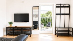 A modern living room with a leather couch, a wooden coffee table, a TV, and a black metal shelf unit. - Airport Messe Apartments (Düsseldorf)