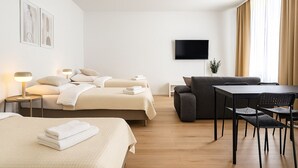 A hotel room with two beds, a sofa, a table, and a TV. - Airport Messe Apartments (Düsseldorf)