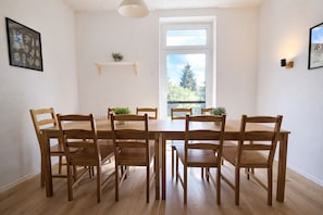 Un coin repas avec une table et des chaises en bois, une fenêtre donnant sur des arbres et une étagère avec une plante.