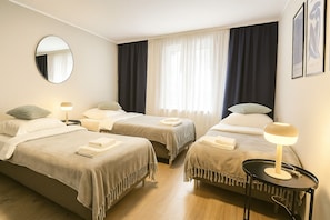 Une chambre d’hôtel avec deux lits, un miroir rond, une table de chevet avec une lampe et une fenêtre avec des rideaux.