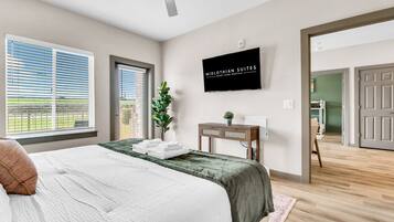 A bedroom with a bed, a flat-screen TV, a desk, and a potted plant.