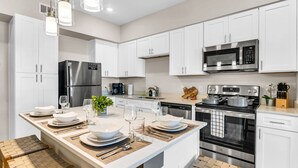 Une cuisine moderne avec des meubles blancs, des appareils en acier inoxydable et un îlot central aménagé en coin repas.