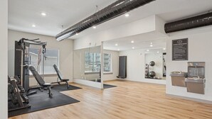 Une salle de sport dotée d’un plancher en bois, d’appareils d’exercice, d’un mur miroir et d’un point d’eau.