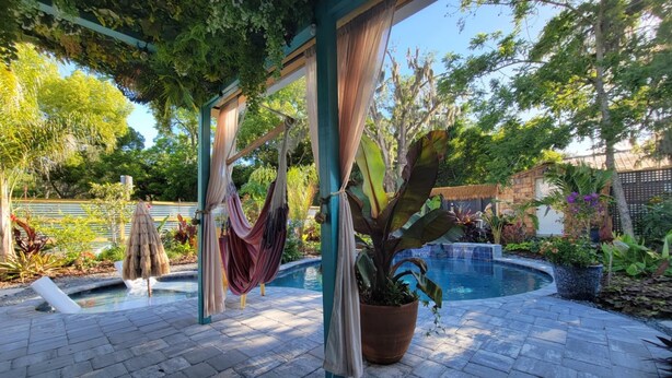 A pool area with a hammock, potted plants, and a pergola.