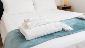 A neatly made bed with white linens, a teal throw blanket, and folded towels on the bed.