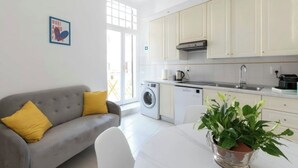 A modern kitchen with white cabinets, a washing machine, and a dining area with a table and a plant.
