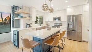 Une cuisine moderne dotée d’un grand îlot central, d’appareils électroménagers en acier inoxydable et de luminaires suspendus.