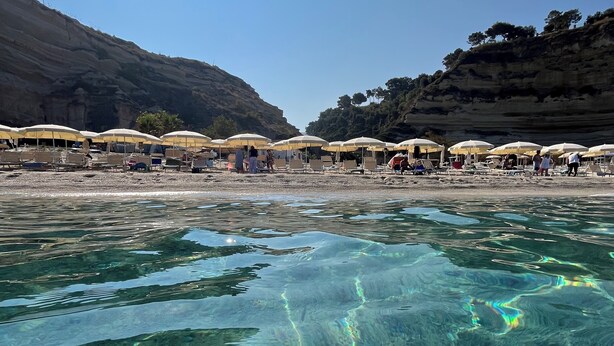 Une plage avec une eau claire, des parasols et des gens.