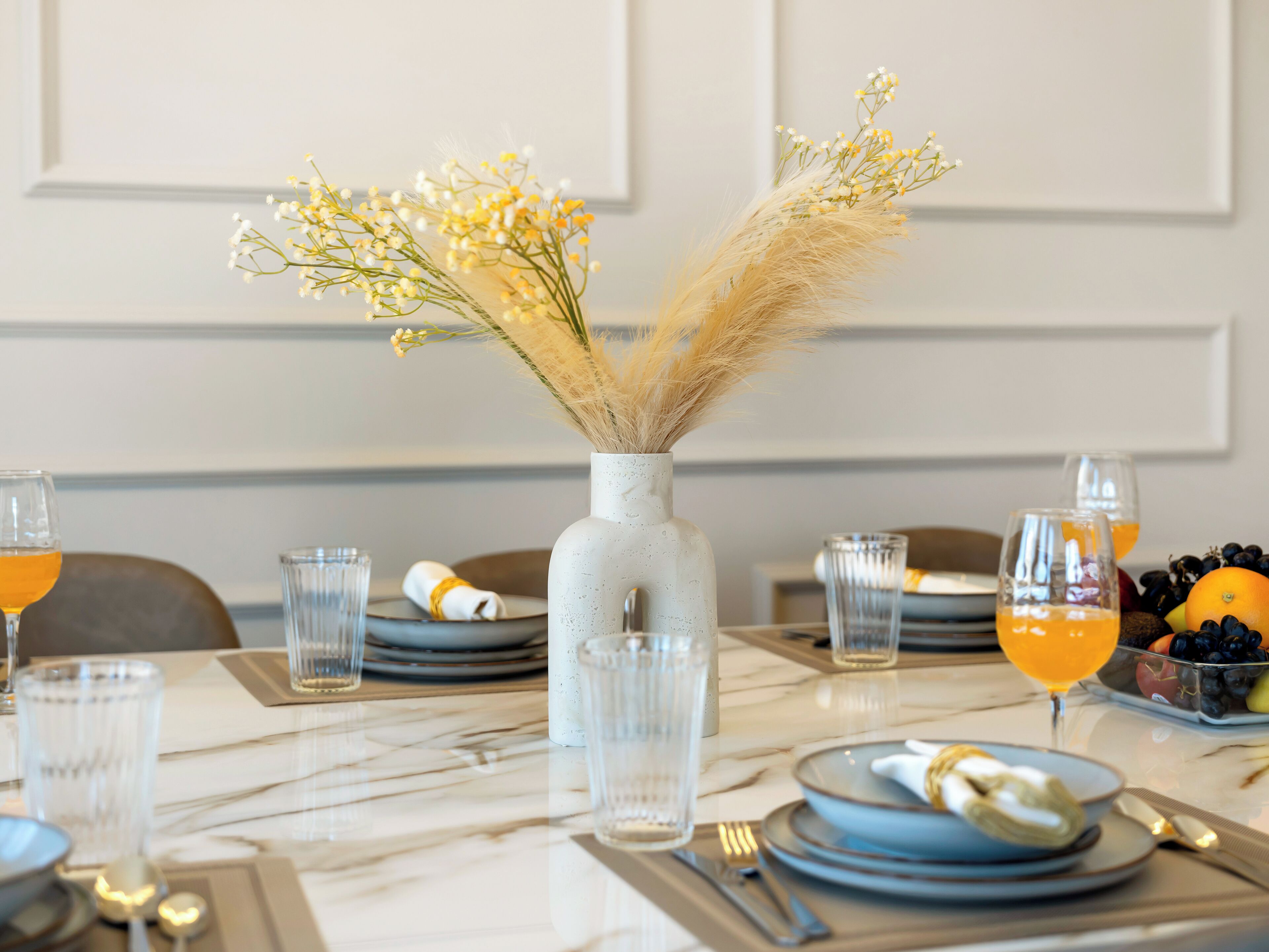 Una mesa de comedor dispuesta con platos, vasos y un florero con flores secas.