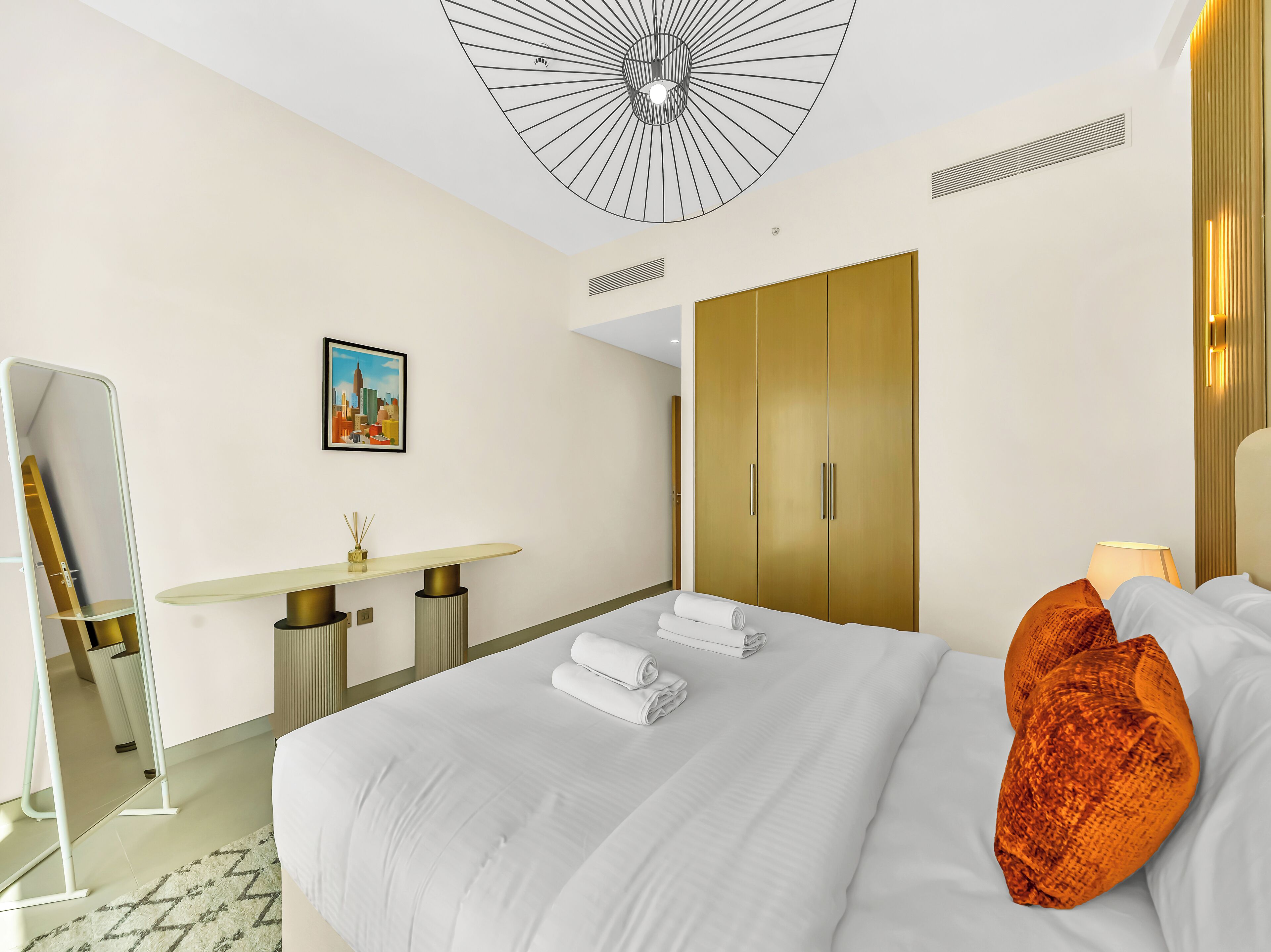 A hotel room with a bed, a desk, a wardrobe, and a painting on the wall.