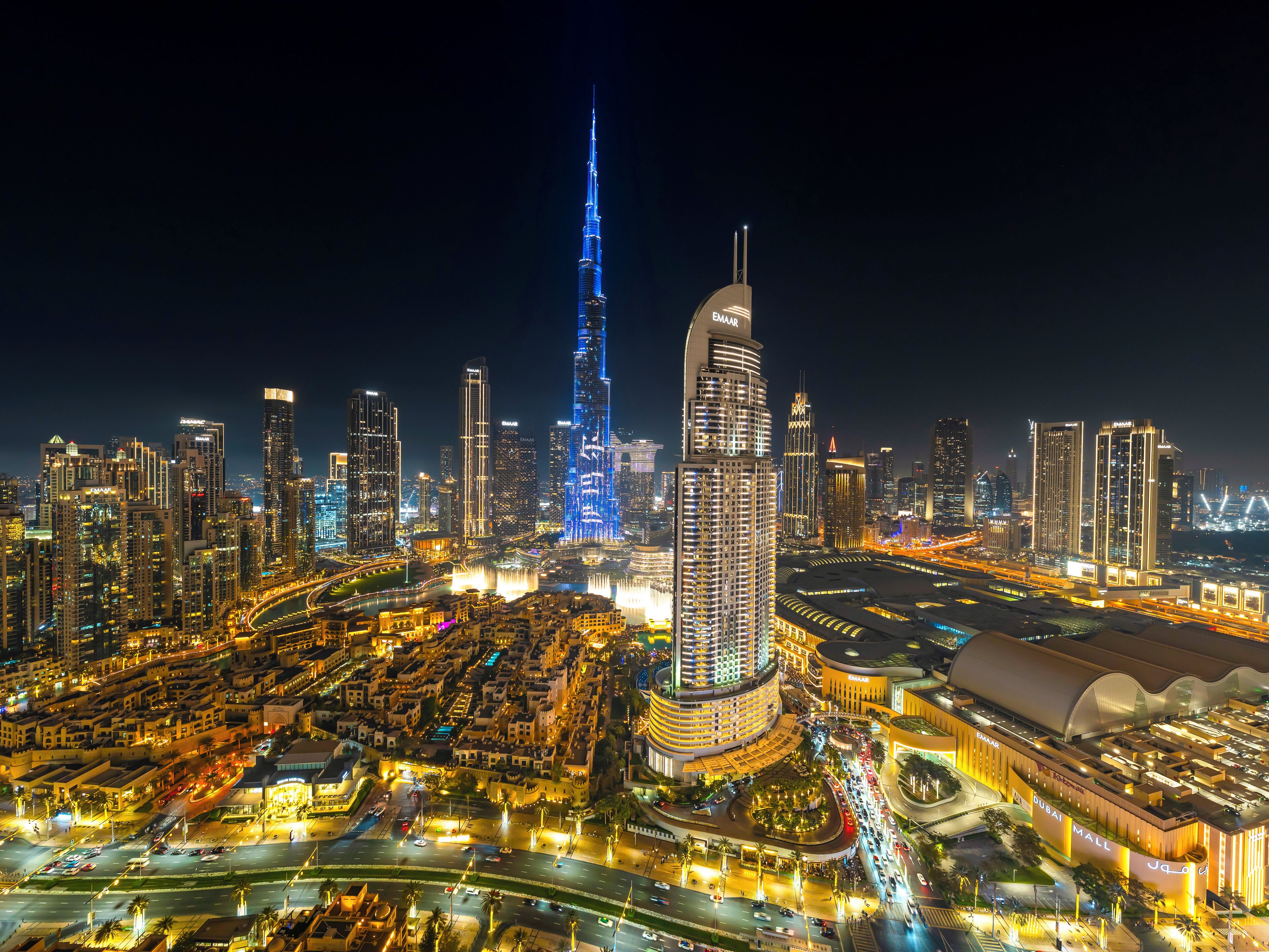 A cityscape at night with prominent skyscrapers, including a tall, illuminated tower and a curved building with a dome.