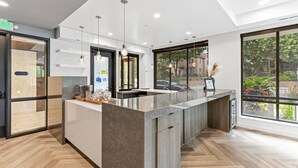 Une cuisine moderne dotée d’un grand îlot central, de luminaires suspendus et offrant une vue sur l’extérieur.