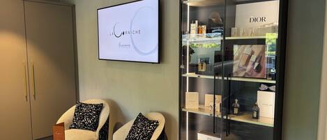 A modern interior with a large display case of luxury brands, two armchairs with patterned cushions, and a wall-mounted screen displaying 'LA CÔRNICHE'.
