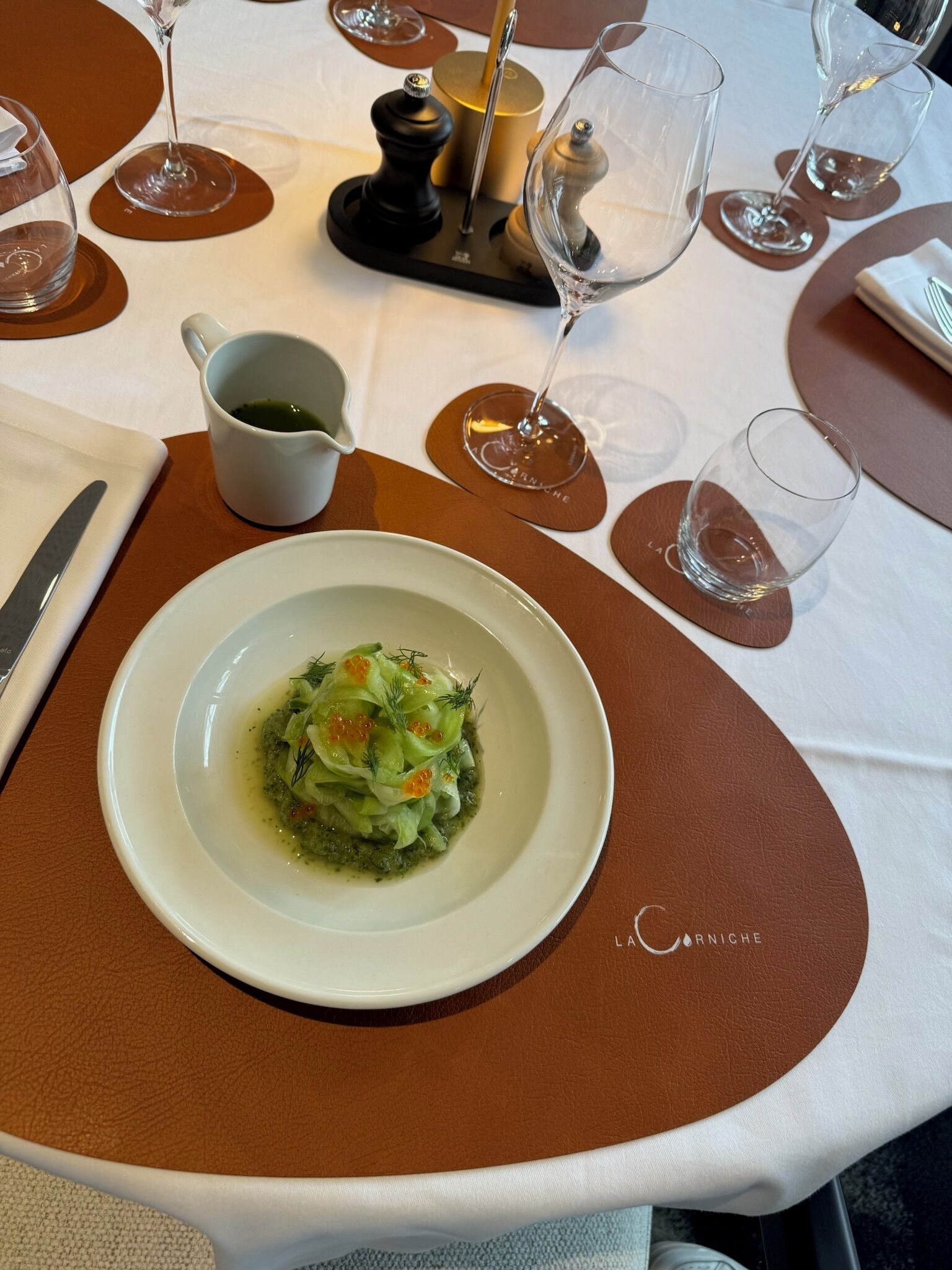 Ein Tisch ist gedeckt mit einem weißen Teller Essen, einer weißen Tasse und mehreren Weingläsern.