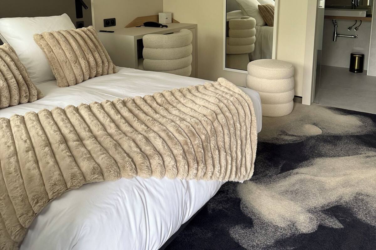 A hotel room with a bed, bedside table, and a mirror.