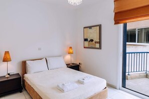 A bedroom with a bed, two bedside lamps, a framed artwork, and a view of an outdoor balcony.