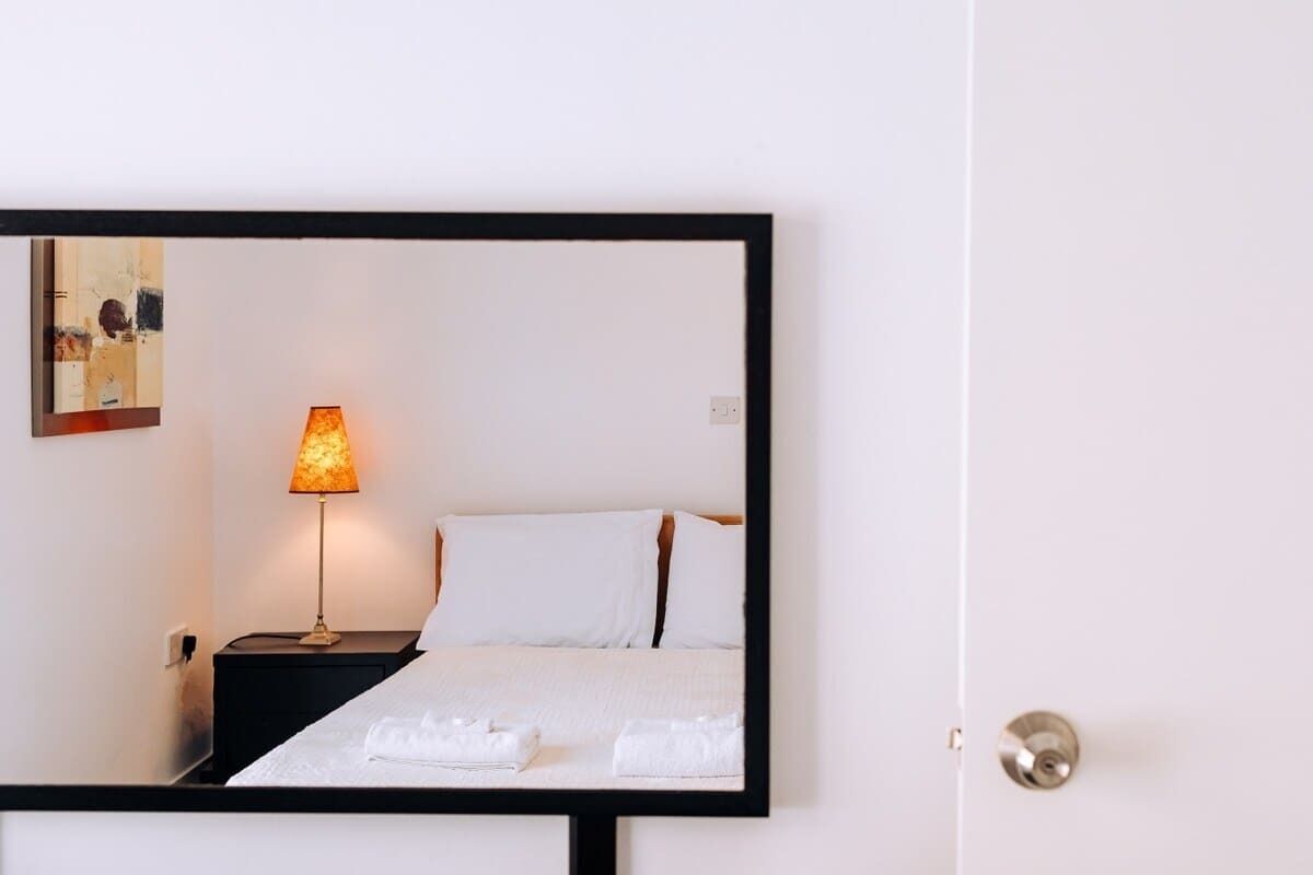 Une chambre d’hôtel avec un lit, une table de chevet avec une lampe et un miroir fixé au mur.