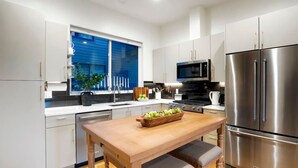 A modern kitchen with white cabinets, stainless steel appliances, a wooden table with a fruit bowl, and a window with blue shutters. - Million $ Rooftop MTN Views -2 King Beds-DT Golden (Golden)