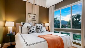 A bedroom with a large bed, two bedside tables with lamps, a view of the outdoors through a large window, and a framed picture on the wall. - Million $ Rooftop MTN Views -2 King Beds-DT Golden (Golden)