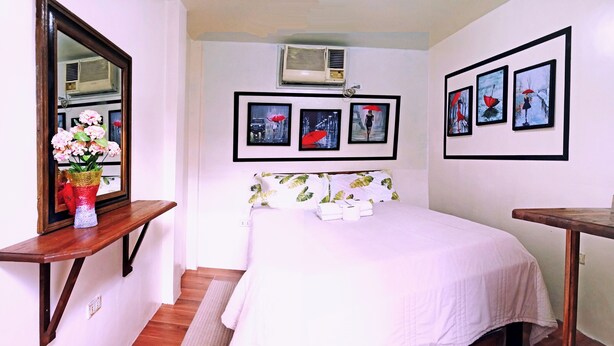 A bedroom with a bed, a bedside table, a mirror, and wall-mounted air conditioning unit. - Room 105 at Liezel's B & B in Palompon / Kalanggaman Island (PALOMPON)