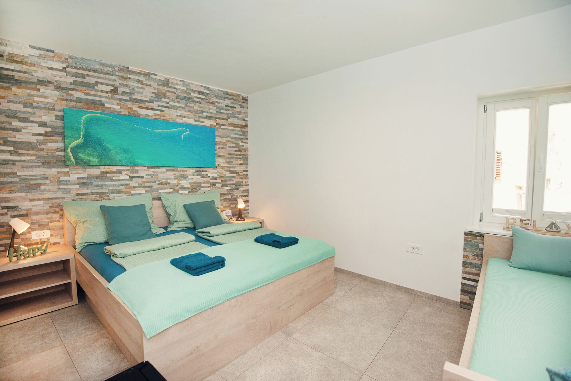 A bedroom with a bed, a nightstand, a wall-mounted TV, and a window.